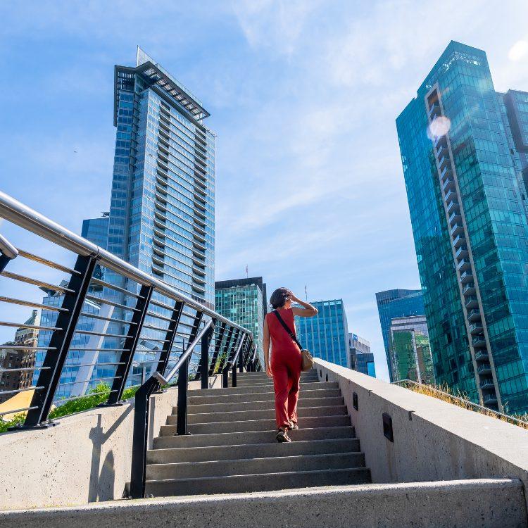 Woman in a red jumpsuit climbing concrete steps between glass towers