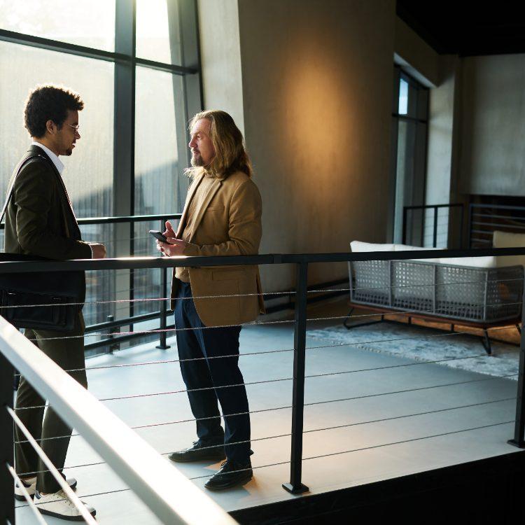 Two colleagues talking on an office mezzanine beside tall windows