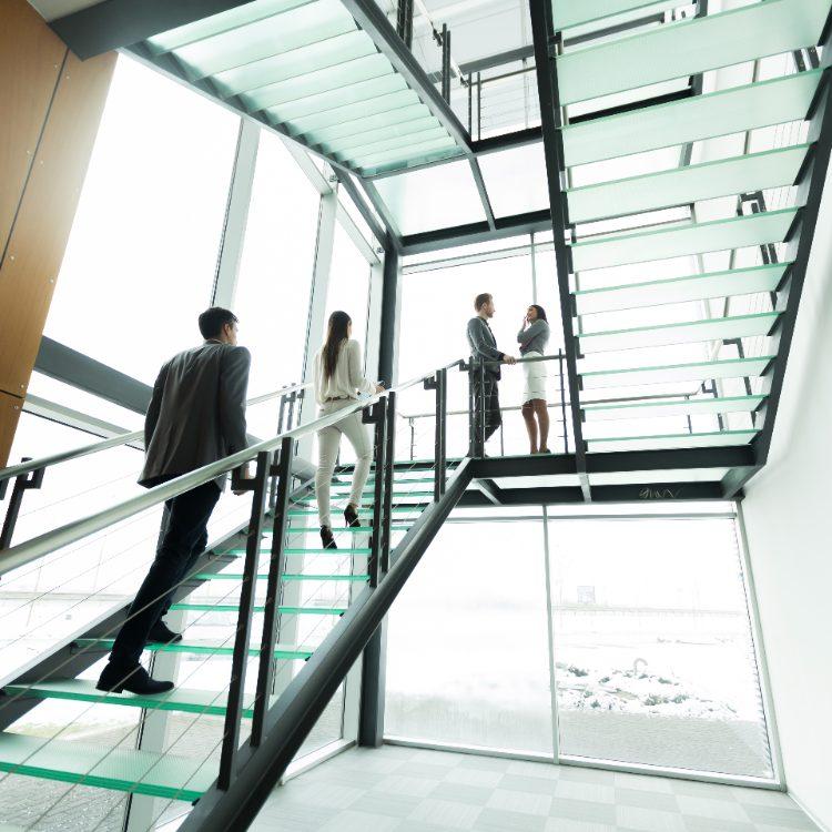 Colleagues climbing a glass staircase while two others talk on the landing above
