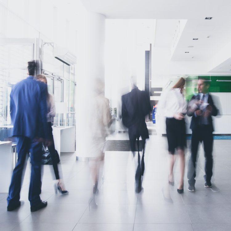 Business people in motion blur walking through a bright office lobby