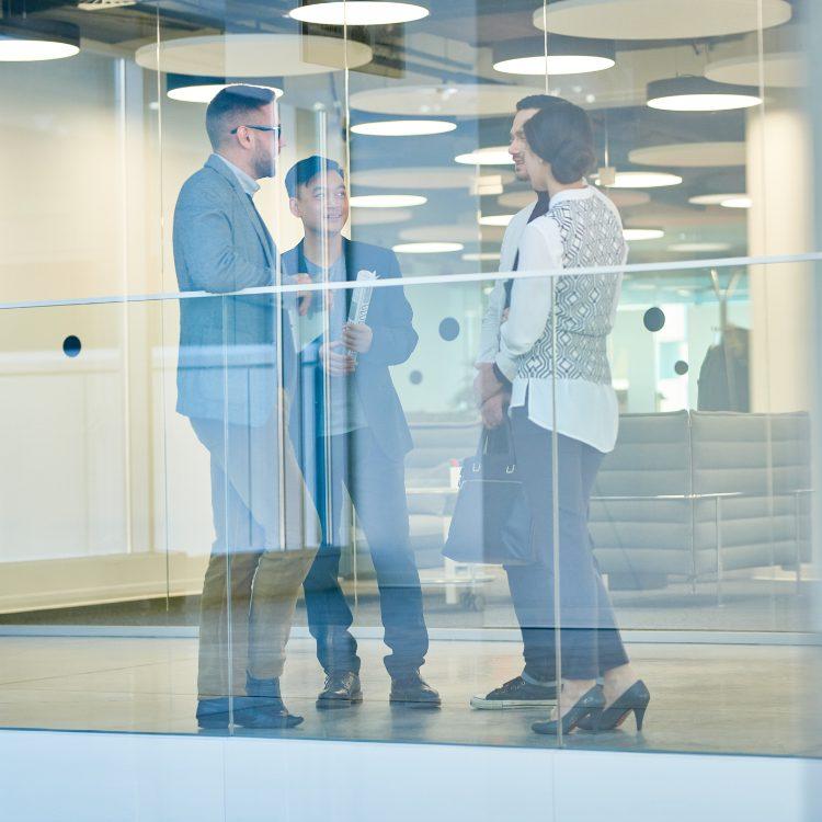 Four colleagues talking behind a glass balustrade in a modern office