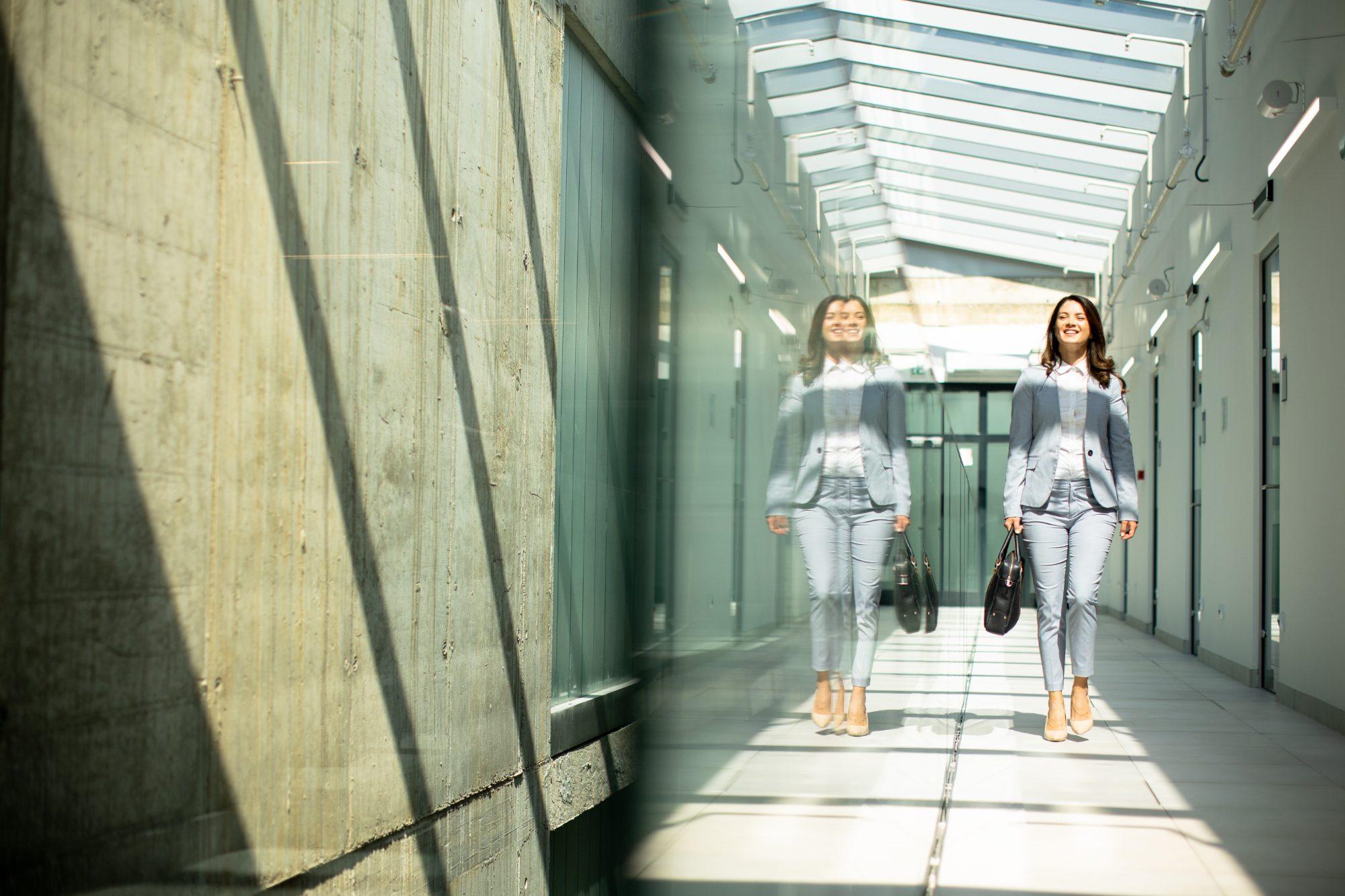 Woman carrying a bag along a sunlit office corridor with a glass roof