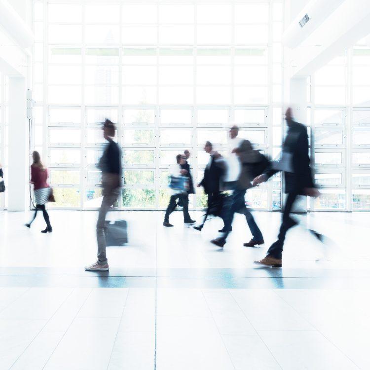 Commuters in motion blur crossing a bright, glass-walled concourse