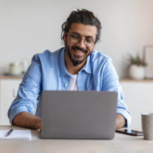 Male employee wearing glasses smiles down at the laptop he's working on in the Momentum office.