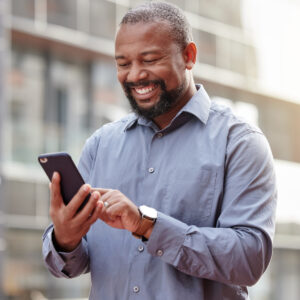 A male holds a smartphone in his hand and smiles down at is as he uses Teams Phone.