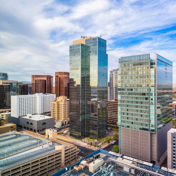 Aerial view of a city skyline featuring modern glass skyscrapers under a partly cloudy sky, with smaller buildings and a parking structure below.