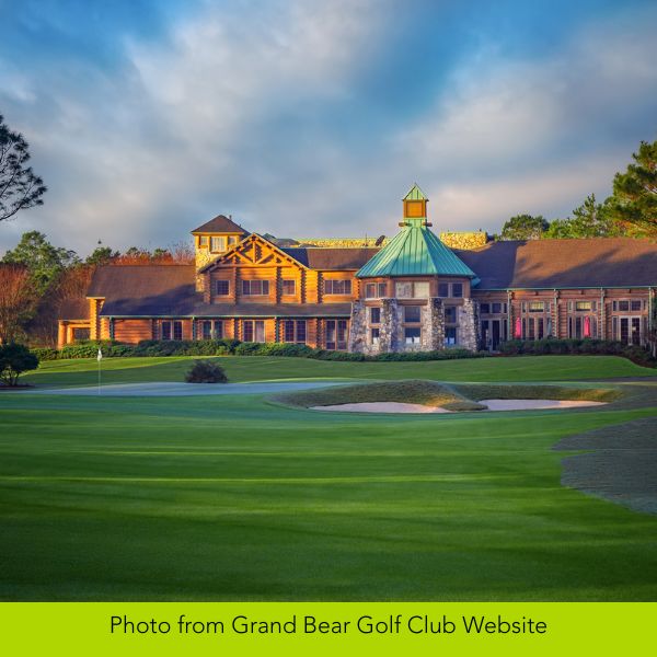 Elegant clubhouse of Grand Bear Golf Club with a green roof, surrounded by lush fairways and under a partly cloudy sky, exuding a serene ambiance.