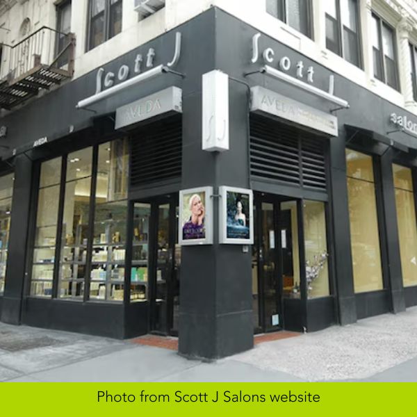 Exterior of Scott J Salon on a city corner, featuring large glass windows with product displays, black facade, and sleek signage. Inviting and stylish.