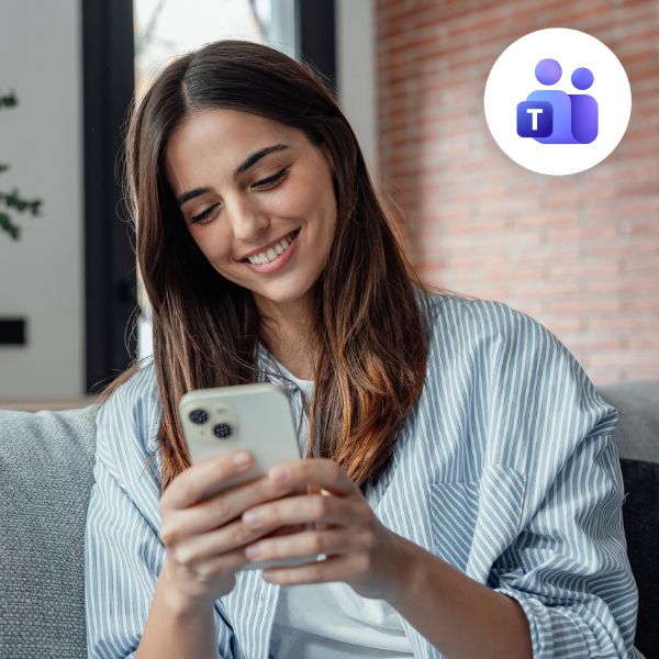 A woman smiles while looking at her smartphone, sitting on a couch in a cozy setting. A Microsoft Teams logo floats in the top-right corner, suggesting communication.