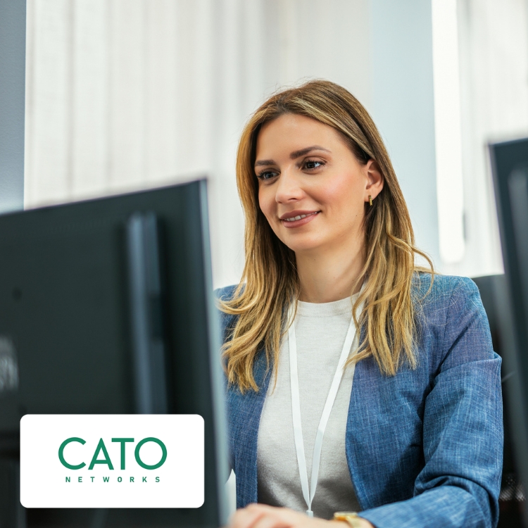 A woman with long blonde hair works at a computer, smiling slightly. She wears a blue jacket and a white lanyard. A logo reads "Cato Networks."