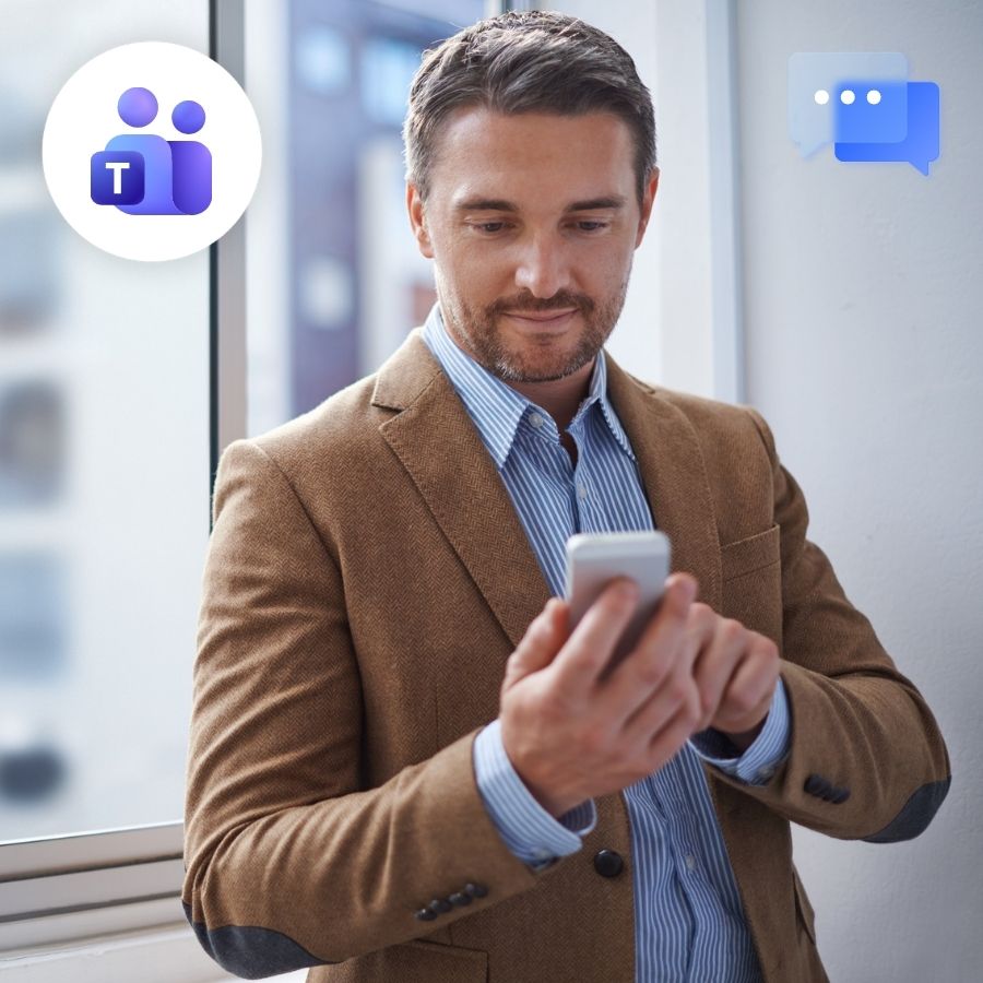 Man in tan blazer texting on a smartphone by an office window, with Microsoft Teams and chat icons.