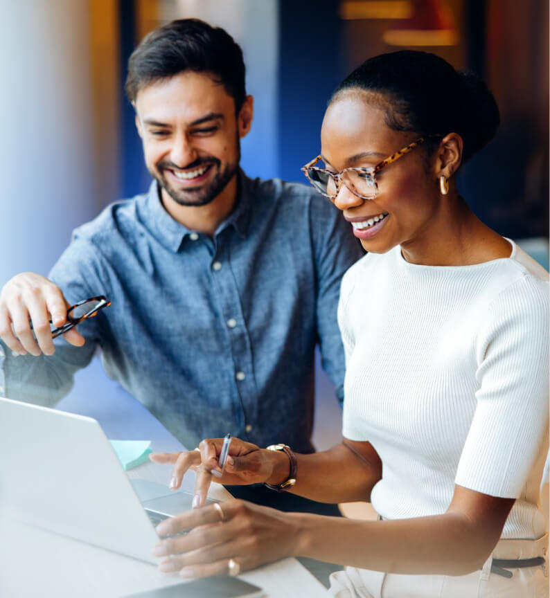 Two colleagues smiling while reviewing content together on a laptop